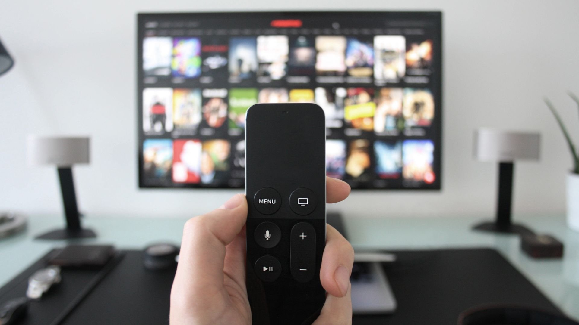 Hand holding remote control in front of TV with streaming service menu